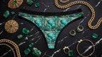 Aesthetic product photography combining an emerald-patterned thong with antique jewelry.